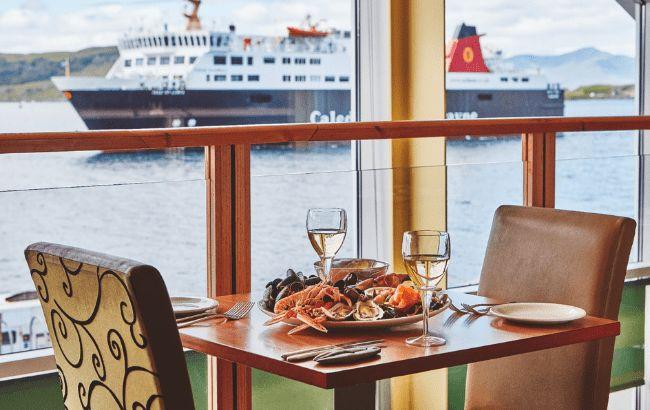 View of passing ship through a window next to a table set for two at a seafood restaurant